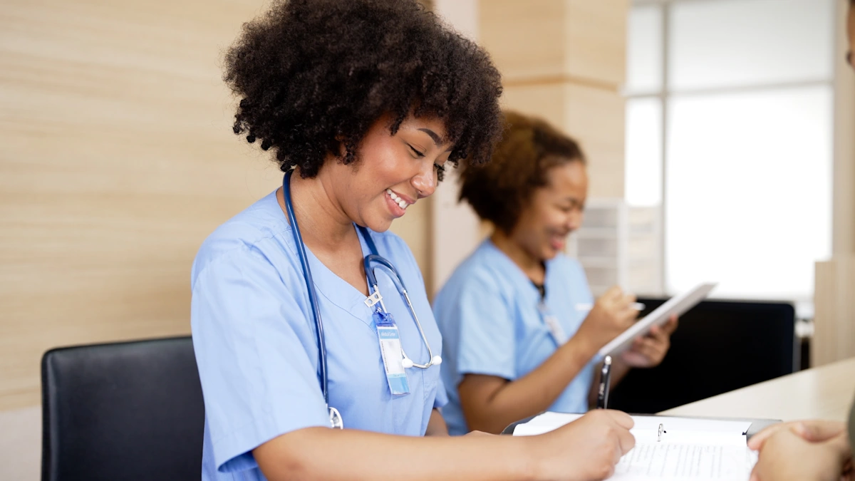 Une femme en blouse bleue assise à côté d'une autre qui écrit quelque chose sur une feuille blanche