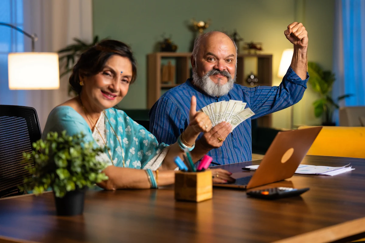 Une femme assise à côté d'un homme qui lève le point en l'air et qui tient des billets d'argent autour d'une table