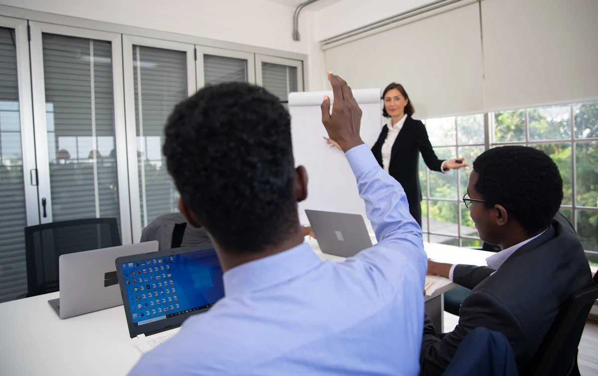 Un jeune homme qui lève la main face à une femme debout près d'un tableau blanc