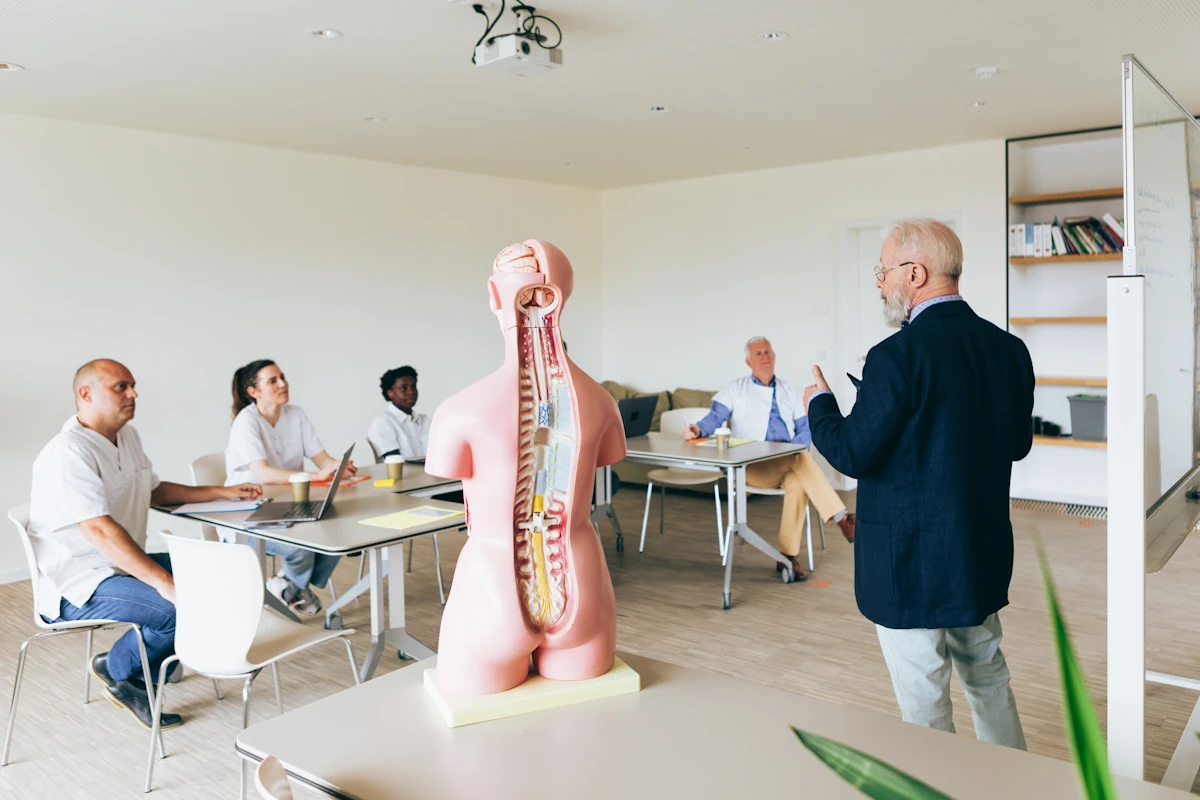 Plusieurs personnes qui suivent une formation avec un homme en veste et devant un mannequin en plastique