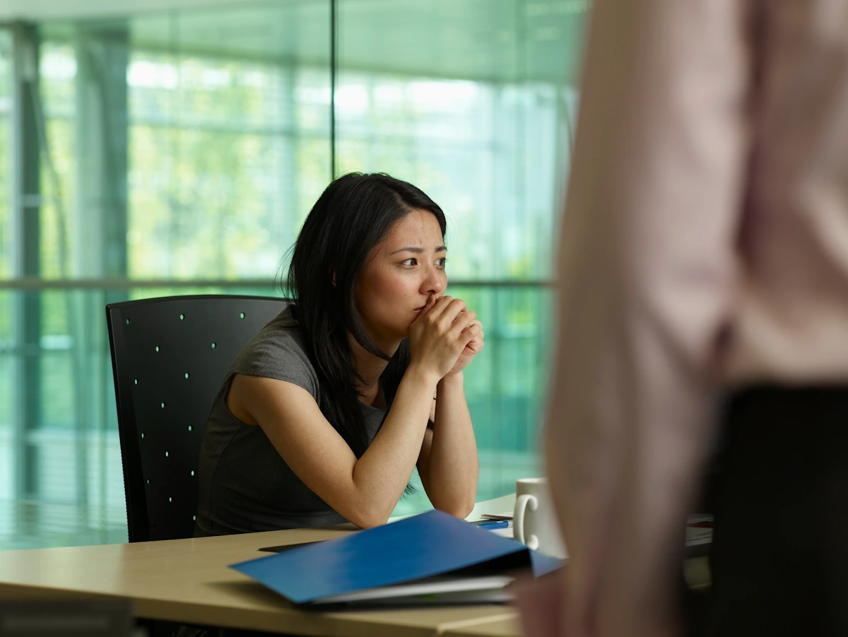 Une femme assise sur son bureau en se couvrant la bouche de ses mains